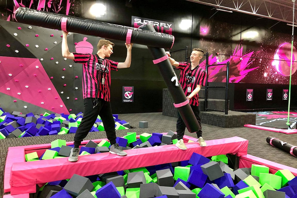 Park attendants play with joust sticks over a battlebeam.