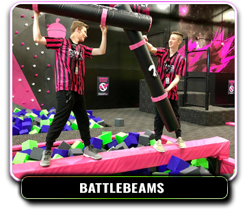 Two park attendants playing with jout sticks on a battle beam above a foam pit.