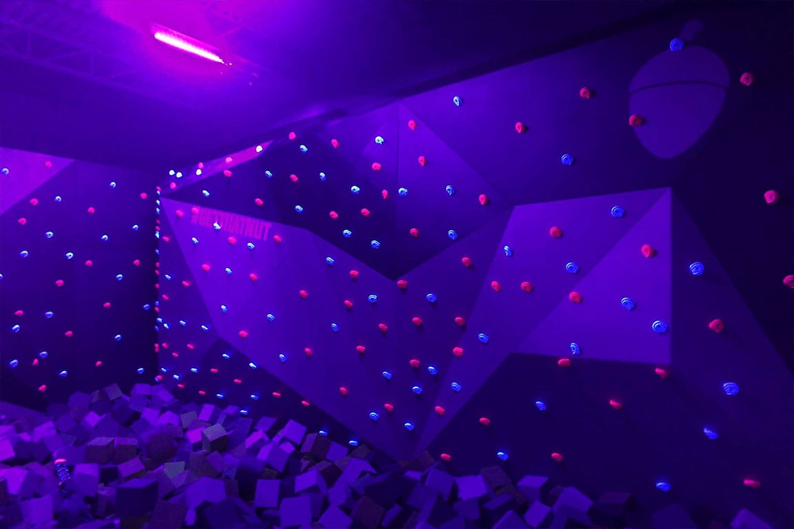 Climbing wall illuminated with neon lights over a foampit.