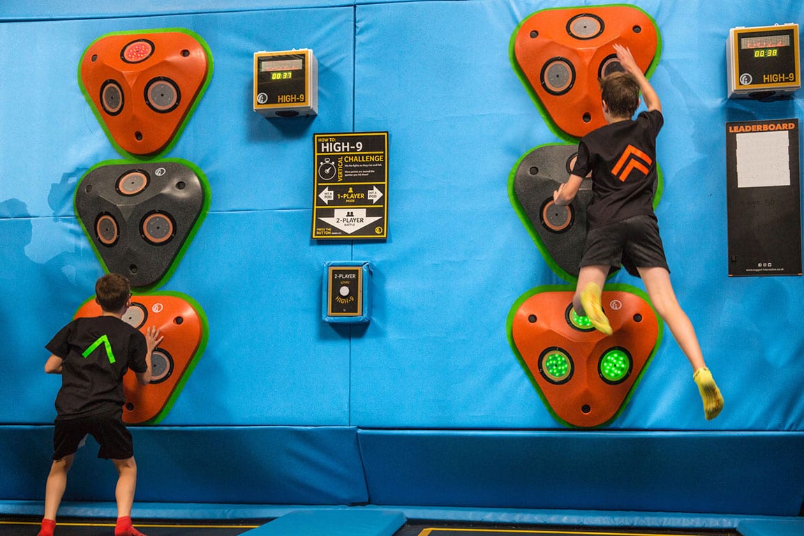 Two children bouncing on trampolines attempting to press buttons to achieve a new high score.