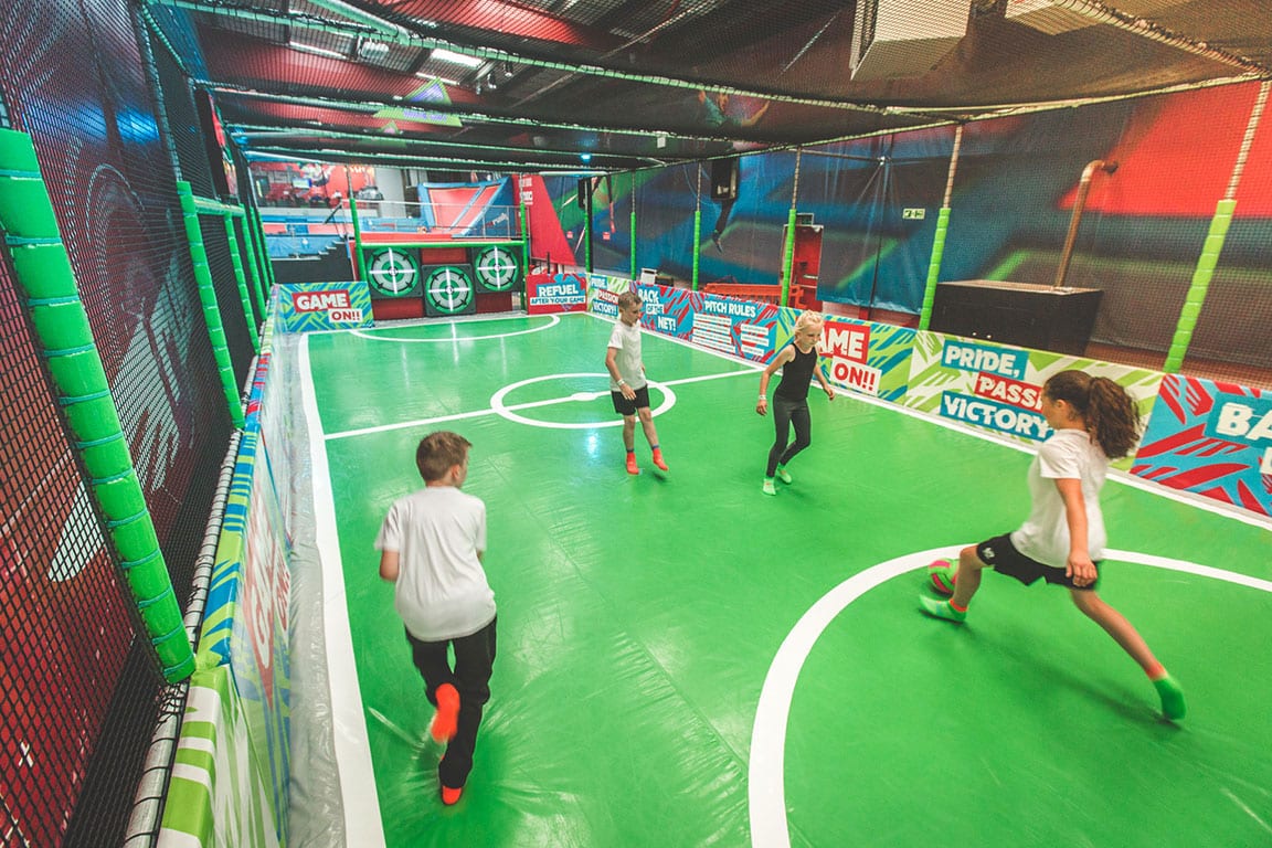 Children playing soccer on a padded surface with targets on the far wall.