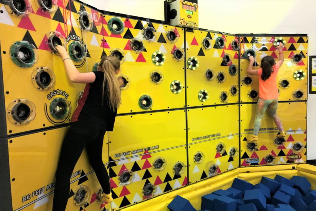 Two children climbing a Rugged Interactive climbing wall with various buttons to press.