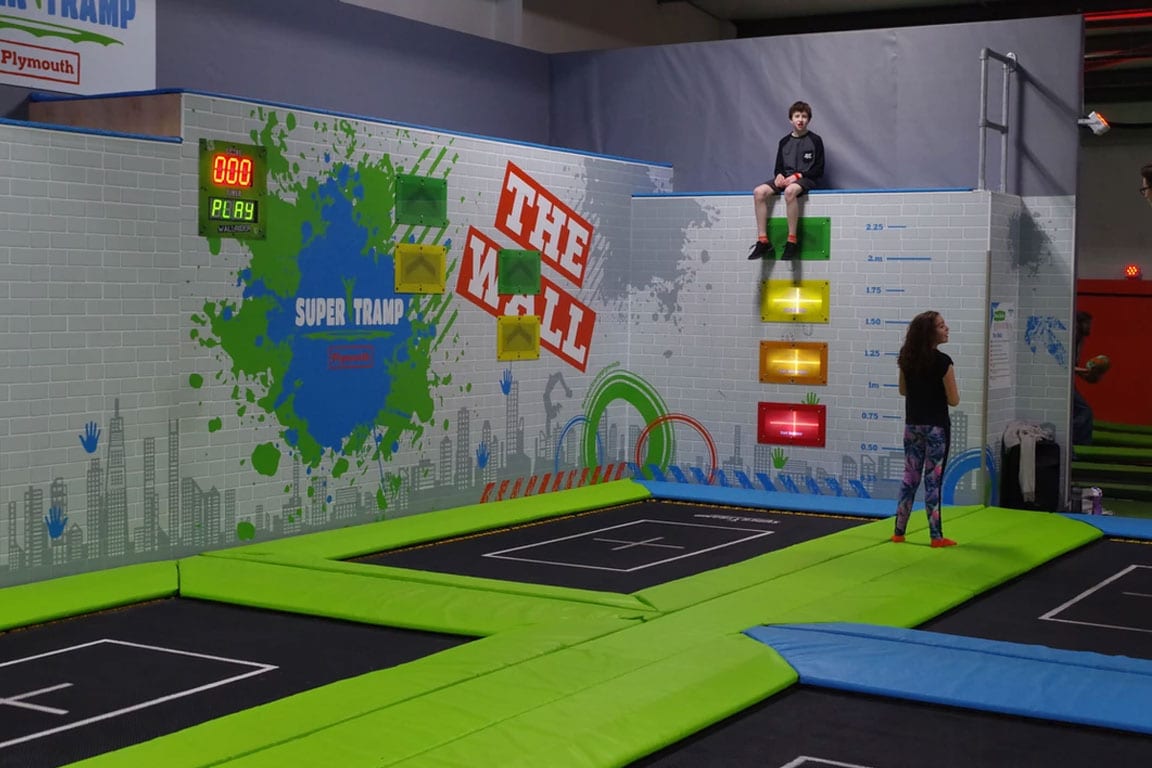 A child sits above a wall with trampolines below him.